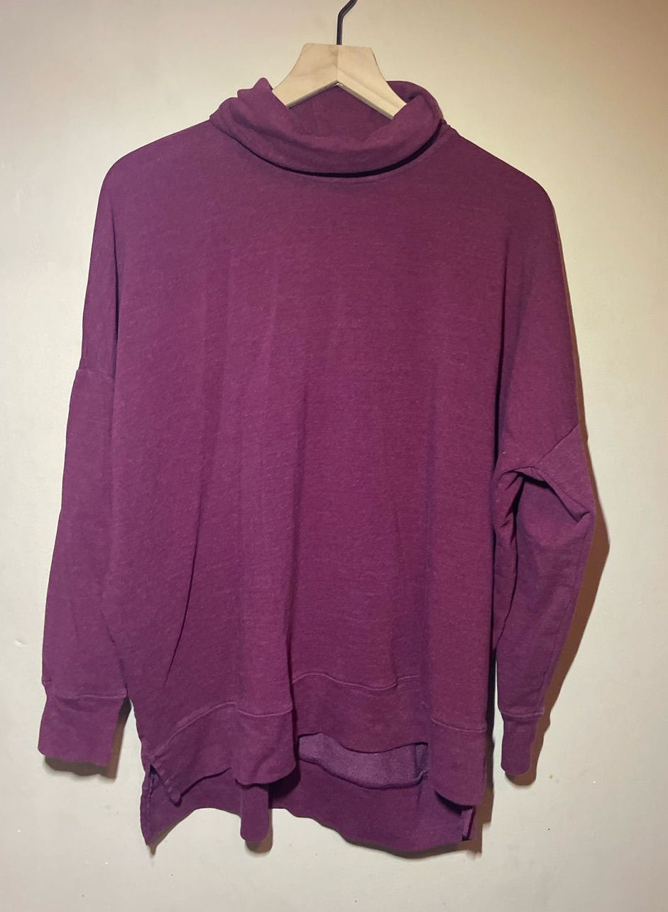 Deep plum-purple cowl-neck sweatshirt hanging against a light wall.