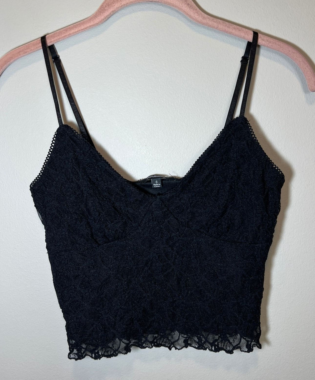 Black floral-lace camisole on a hanger, with a scalloped neckline and adjustable straps.
