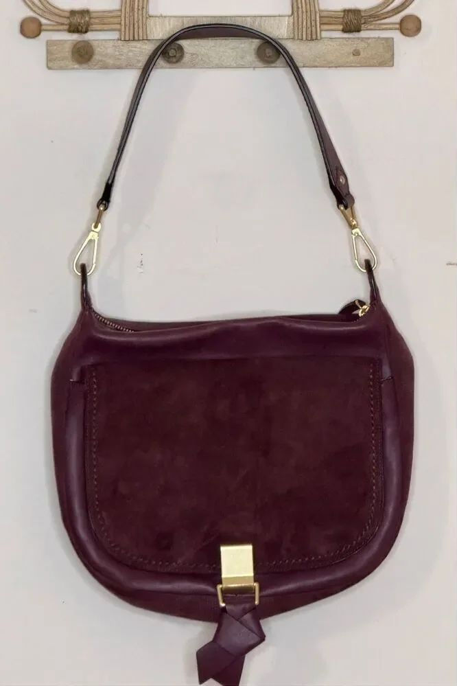 Plum leather shoulder bag with subtle grain and gold-tone hardware against a light background.