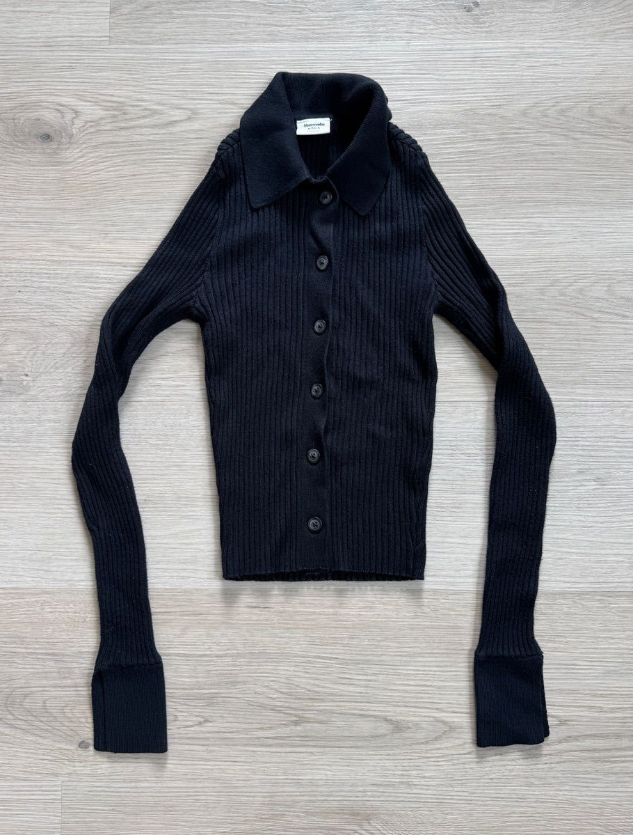 Black ribbed button-front cardigan laid flat, with a fitted waist and slim sleeves.