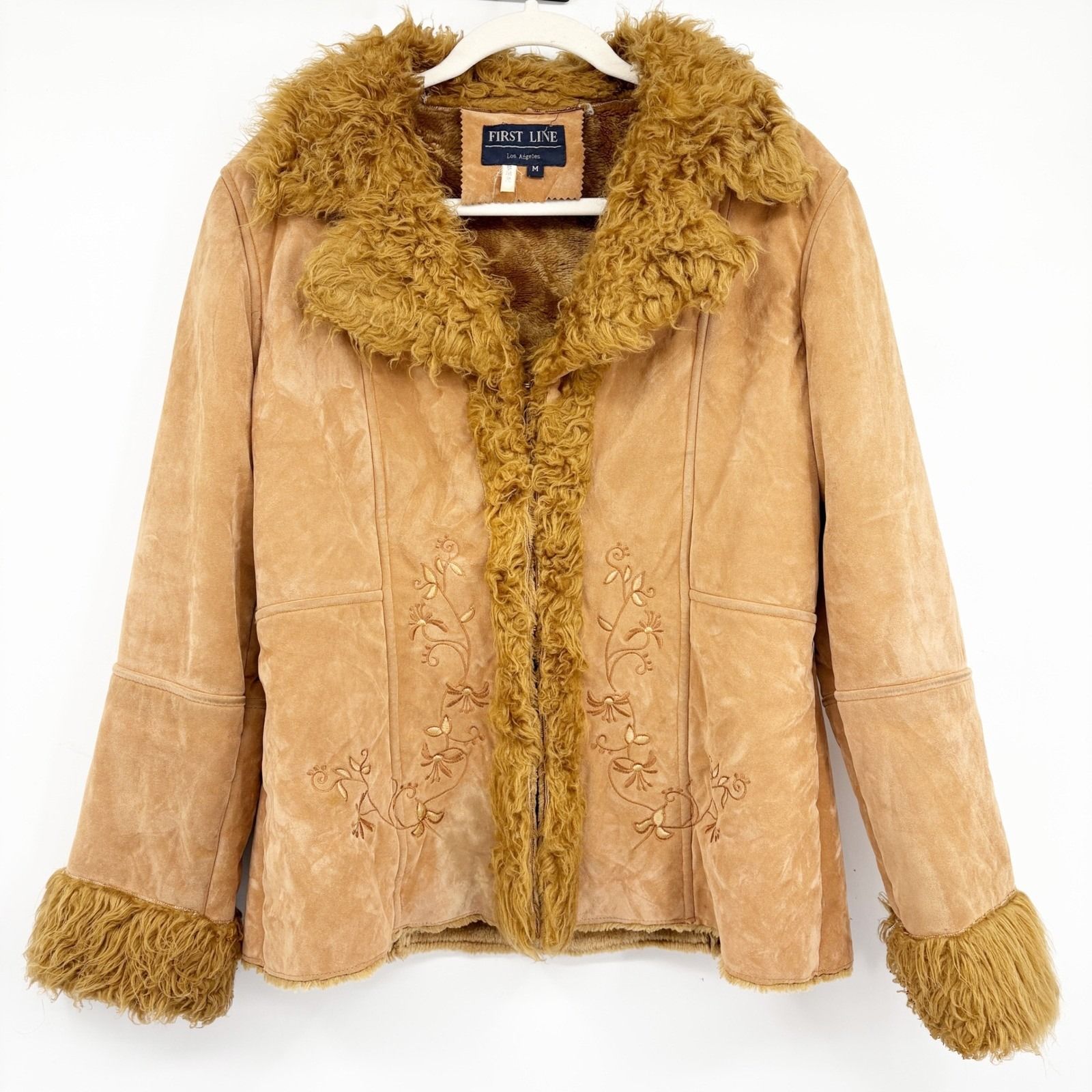 Tan suede-look jacket with a shaggy golden-brown collar and plush cuffs, displayed on a hanger.