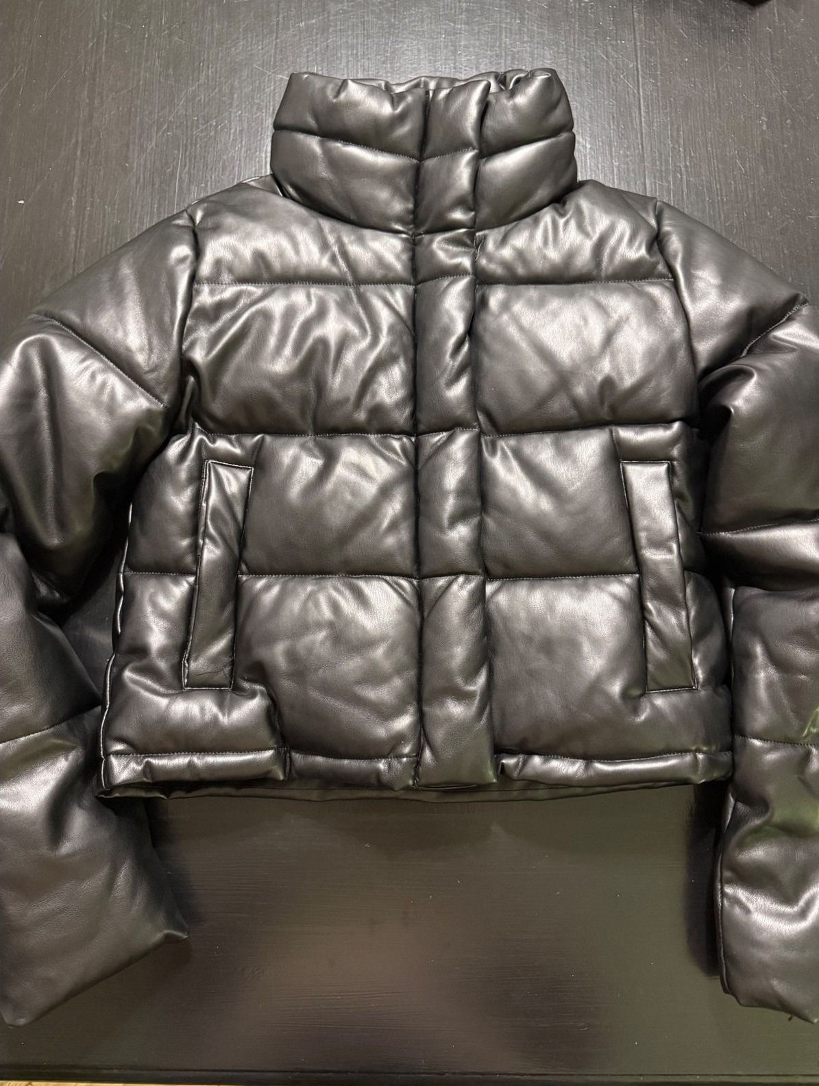 Black cropped faux-leather puffer jacket laid flat with its wide funnel collar upright.