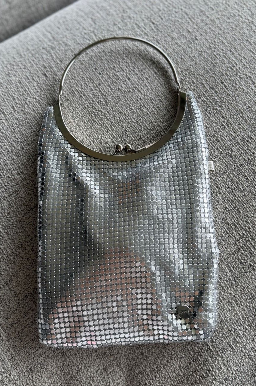 Silver chainmail evening bag with linked mesh and a rounded handle against gray fabric.