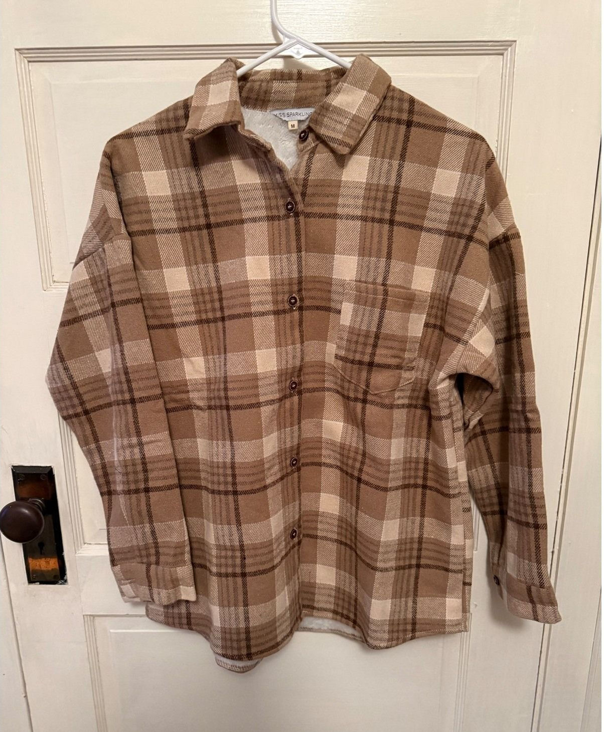 Brown-and-cream plaid flannel shirt hanging against a white door.
