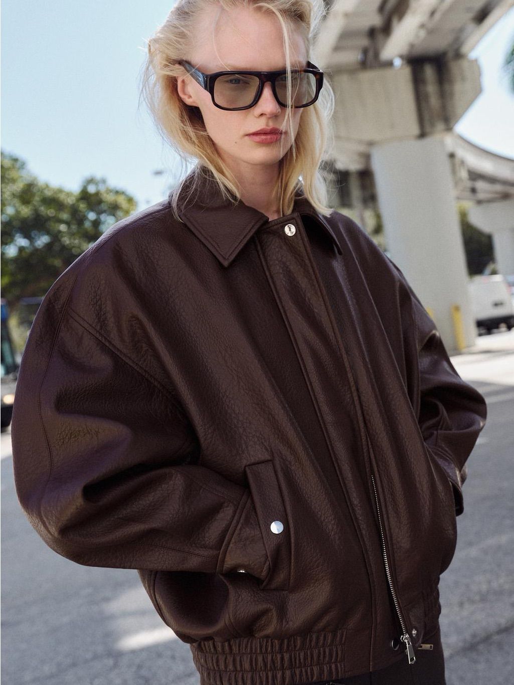Espresso-brown faux-leather bomber jacket with broad shoulders, rounded sleeves, and a gathered hem.