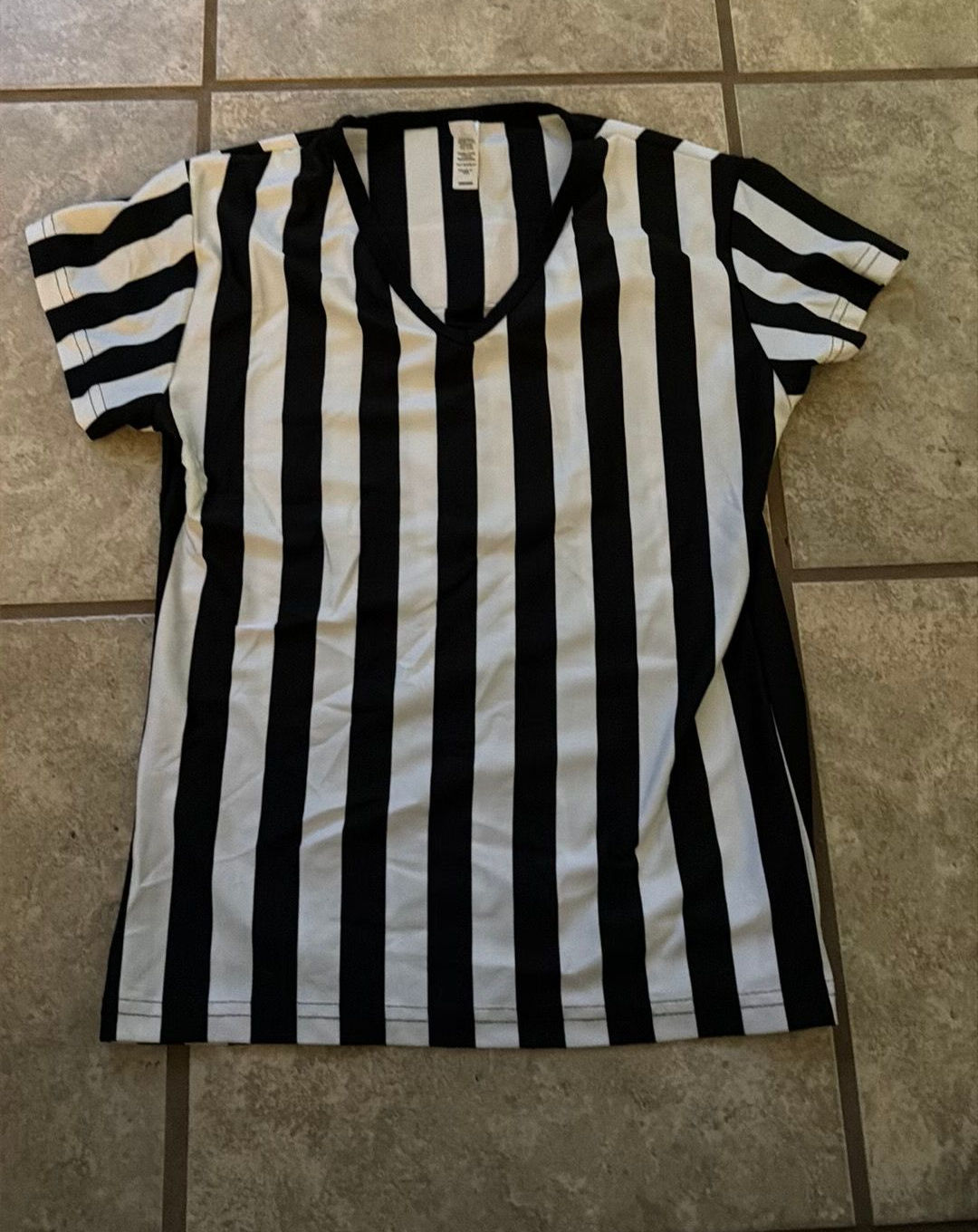 Short-sleeved referee shirt laid flat, showing broad vertical black-and-white stripes.