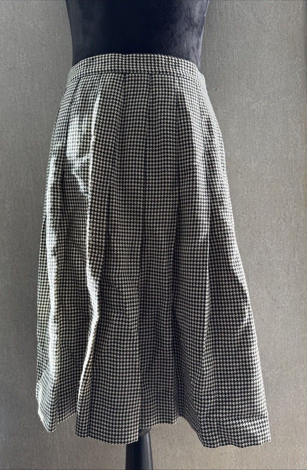 Black-and-white houndstooth pleated midi skirt hanging with its waistband and pleats visible.
