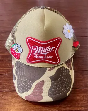 camouflage-patterned Miller High Life trucker hat featuring embroidered patches. thumbnail 1