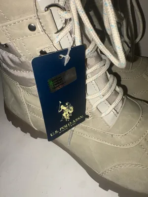 U.S. Polo Assn. Women's Yvonne Snow Boots in an "Oatmeal" or beige colorway. These mid-calf winter boots feature a duck-toe rubber shell base for slush protection, a quilted canvas shaft, traditional lace-up closure, and a plush faux-fur collar trim. A signature metallic logo plaque is attached to the side strap thumbnail 2