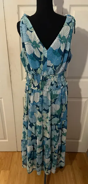 Beautiful blue floral print maxi dress has a smocked elastic waist and a tiered skirt. This sleeveless garment is designed with a V-neckline and adjustable tie-shoulder straps. The fabric is a lightweight material with subtle metallic gold thread accents throughout. thumbnail 2