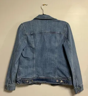 The Old Navy Blue Denim Trucker Jacket is a classic button-up long sleeve jacket in a traditional trucker style. Made from denim, manufactured in Bangladesh.Pit to pit: 18 in. Length: 20 in. Pre-owned with no visible wear. Buttons are all intact and the jacket lays flat with no distortion thumbnail 2