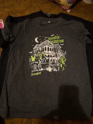 Explore the eerie allure of the Haunted Mansion with this Disney tee. Features a striking graphic in charcoal and neon green. Ideal for theme park enthusiasts. thumbnail 1