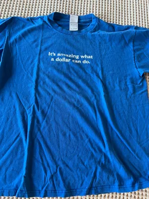Comfortable blue short-sleeve shirt with white centered text that reads "It's amazing what a dollar can do." Soft, breathable cotton blend for everyday wear. Crew neckline and relaxed fit for easy styling. Blue color adds a bold pop to casual outfits. thumbnail 1