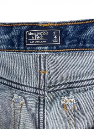 Abercrombie & Fitch Mom Cutoff High Rise Denim Shorts Womens 27 Abercrombie & Fitch high rise cutoff mom shorts in a distressed medium wash. Raw frayed hemline with classic 5 pocket styling and zip fly button closure. Modern release design features a clean back waist without traditional leather logo patch. Rigid 100 percent cotton denim build with structured vintage silhouette. Excellent preowned. No flaws, stains, or unintentional tears. Measurements Flat Lay: Waist 14.25 in Rise 10 in Inseam 2 in Hips 17 in thumbnail 4