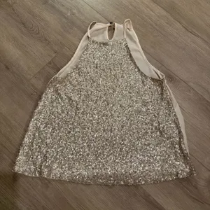 Altar'd State Tan Sequined Halter Top - Women's Size Small Elevate your next night out with this stunning Altar'd State halter top. Featuring a dazzling sequined front in a versatile tan/champagne hue, this piece offers a beautiful shimmer and a flattering, flowy silhouette. The back is crafted from a smooth, lightweight fabric with a stylish keyhole closure at the neck. • Brand: Altar'd State • Size: Women’s Small • Color: Tan / Champagne • Condition: Like new, excellent condition • Style: Sequined front, halter neck, keyhole back Perfect for parties, concerts, or holiday events! thumbnail 1