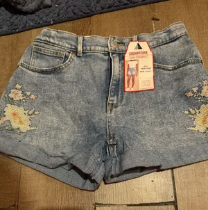 Signature Levi Strauss light blue denim shorts with delicate floral embroidery. Comfortable high-rise fit designed for everyday wear. Soft, faded blue wash that pairs easily with casual tops. Floral detailing adds a feminine touch. thumbnail 1