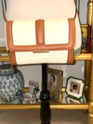 White and brown crossbody bag with adjustable strap. The design features a front flap with a brown leather detail and a clip closure. thumbnail 2