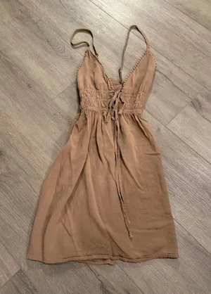 Wild Fable Tan Pom-Pom Trim Mini Dress - Size XS Get ready for sun-drenched days with this adorable Wild Fable mini dress. Featuring a neutral tan hue, this piece stands out with its delicate pom-pom trim along the neckline and a boho-inspired lace-up front with tassel details. The smocked waist ensures a flattering, flexible fit, while the lightweight fabric makes it perfect for beach trips or brunch. • Condition: Like new / Excellent • Size: Women’s XS • Style: Halter neckline with adjustable spaghetti straps • Color: Tan/Beige Smoke-free home. Fast shipping! thumbnail 1