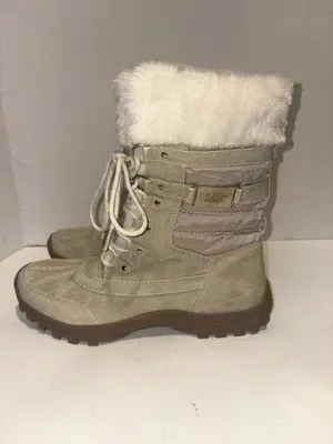 U.S. Polo Assn. Women's Yvonne Snow Boots in an "Oatmeal" or beige colorway. These mid-calf winter boots feature a duck-toe rubber shell base for slush protection, a quilted canvas shaft, traditional lace-up closure, and a plush faux-fur collar trim. A signature metallic logo plaque is attached to the side strap thumbnail 4