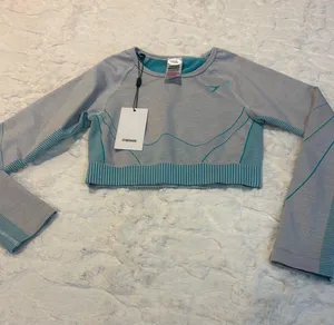 Gymshark Women's Teal and Gray Long Sleeve Crop Top Size Small . Stylish long sleeve crop top by Gymshark. Features a sleek teal and gray design. Perfect for workouts.. NWT thumbnail 2