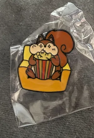 Squirrel on sofa eating popcorn Enamel Pin Orange thumbnail 1