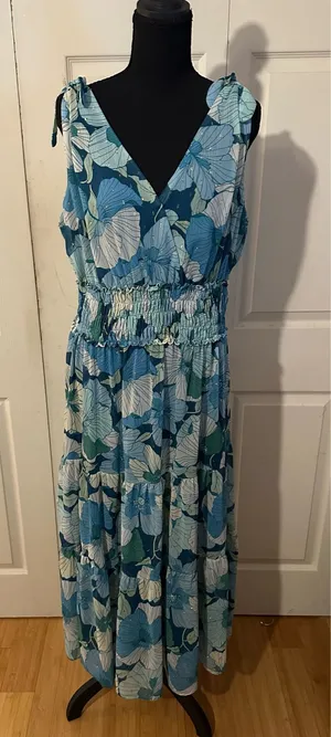 Beautiful blue floral print maxi dress has a smocked elastic waist and a tiered skirt. This sleeveless garment is designed with a V-neckline and adjustable tie-shoulder straps. The fabric is a lightweight material with subtle metallic gold thread accents throughout. thumbnail 1