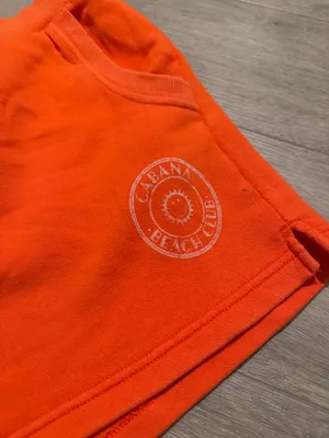 Aerie x Smiley Orange Sweat Shorts - Size XL (Like New) Description: Upgrade your loungewear with these vibrant, bright orange Aerie x Smiley fleece sweat shorts! As seen they feature a comfy elastic waistband, handy side pockets, and a cute "Cabana Beach Club" smiley logo on the left hem. Condition: Excellent, like-new condition with no visible flaws Size: XL / TG Details: Soft fleece lining, perfect for beach days or casual lounging. Close-up of the graphic logo can be found Super cozy and ready for a new home! Fast shipping. thumbnail 2