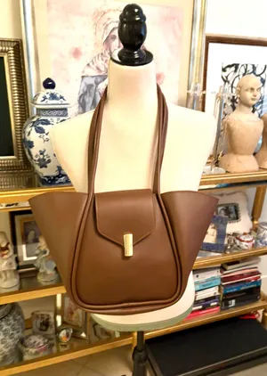 This brown bag features a minimalist design with gold details and a spacious structure. Made from 100% polyurethane, it has a magnetic closure with a gold-tone latch. Designed as a tote or shoulder bag, it's versatile for everyday use or travel. thumbnail 1
