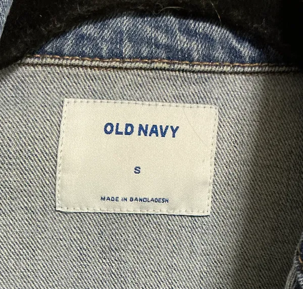 The Old Navy Blue Denim Trucker Jacket is a classic button-up long sleeve jacket in a traditional trucker style. Made from denim, manufactured in Bangladesh.Pit to pit: 18 in. Length: 20 in. Pre-owned with no visible wear. Buttons are all intact and the jacket lays flat with no distortion - Image 3