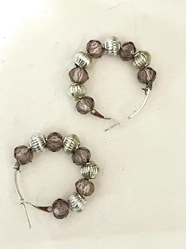 These handmade beaded hoop earrings feature a unique combination of purple, gray, and silver tones. The faceted beads add a touch of bohemian style, making them a perfect gift for someone who loves one-of-a-kind accessories. The handmade quality adds a personal touch to these earrings, making them a standout piece for any jewelry collection. - Image 4